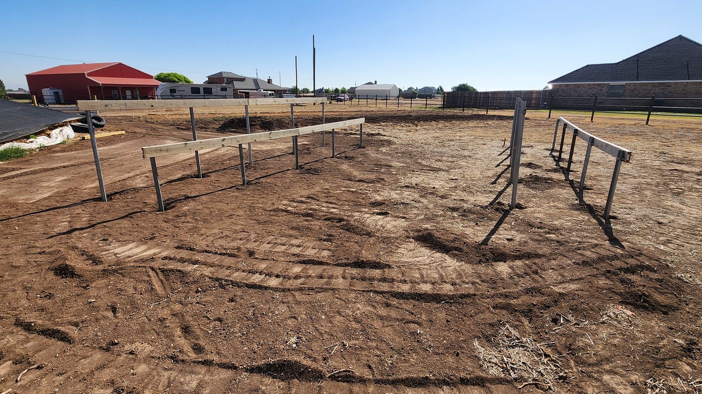 Galvanized posts and timber rails set in graded ground, the beginning of a ground-mount solar frame