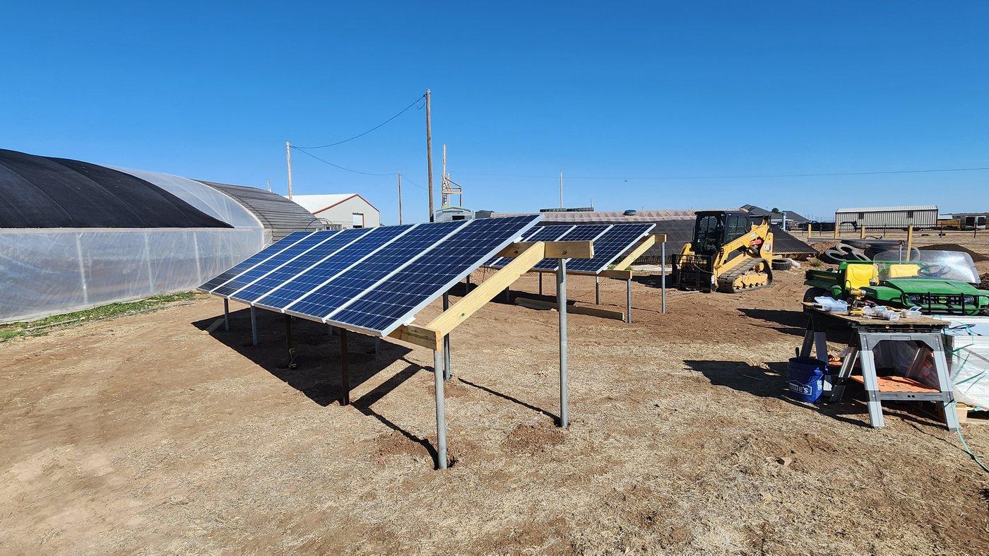 Completed ground-mount solar array beside a greenhouse with a skid steer and tools on site
